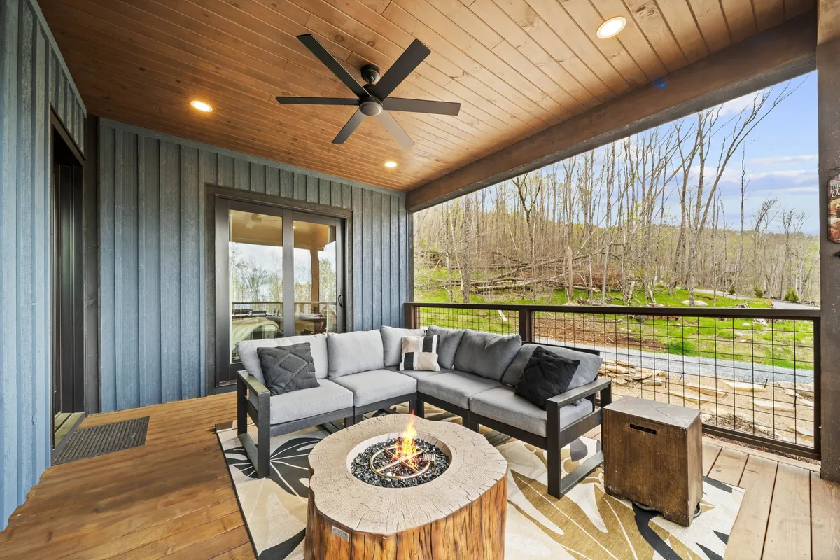A dedicated fire pit area with comfortable outdoor seating beneath a wooden ceiling, overlooking a scenic landscape. The design enables groups to gather around the fire while taking in sunset views and mountain air.
