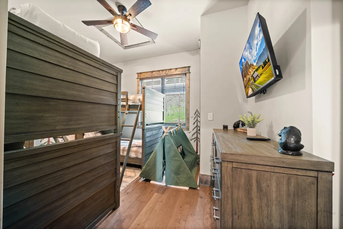 A playful bunk room with twin-over-twin bunk beds, a wooden dresser, a TV mounted on the wall, and a whimsical teepee tent in the corner. The decor is inviting for children, offering both sleep and imaginative play spaces.