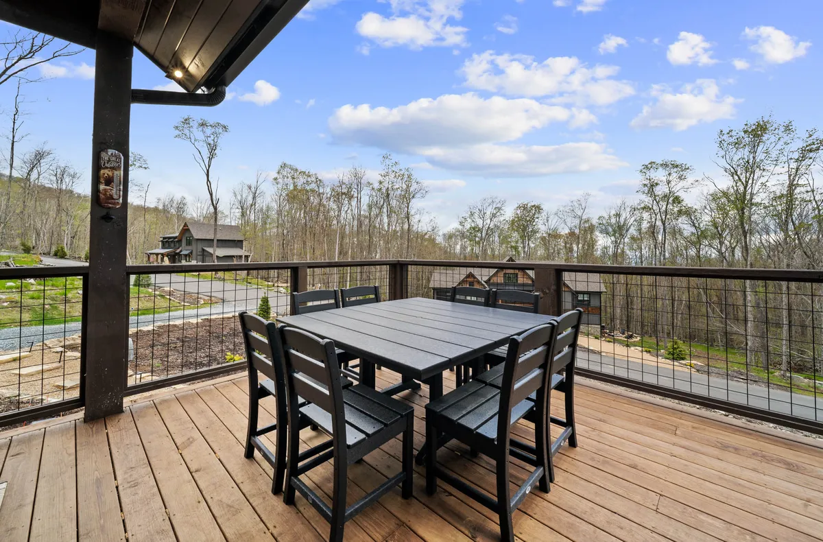 This image features a wooden outdoor table and black chairs set against a scenic view, ideal for al fresco dining or social gatherings. The landscape in the background suggests the changing seasons through the vivid outdoor scenery.