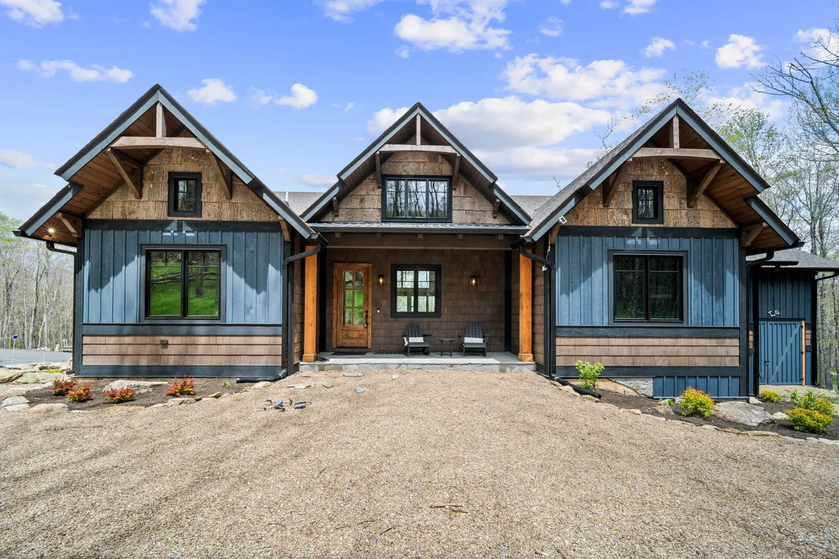 The front porch of the home features a charming wooden door and gabled roof, set against a scenic backdrop. The porch beckons guests to relax and take in sunset views or enjoy a peaceful evening of stargazing.