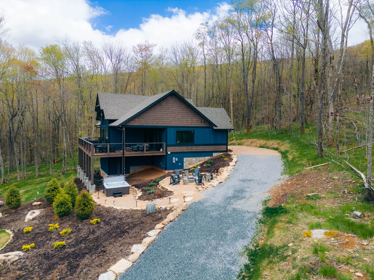 This image features the house's exterior, focusing on the patio area and driveway surrounded by a tranquil natural landscape. The patio is inviting for outdoor dining, relaxing, or socializing, making it a versatile gathering space for families.