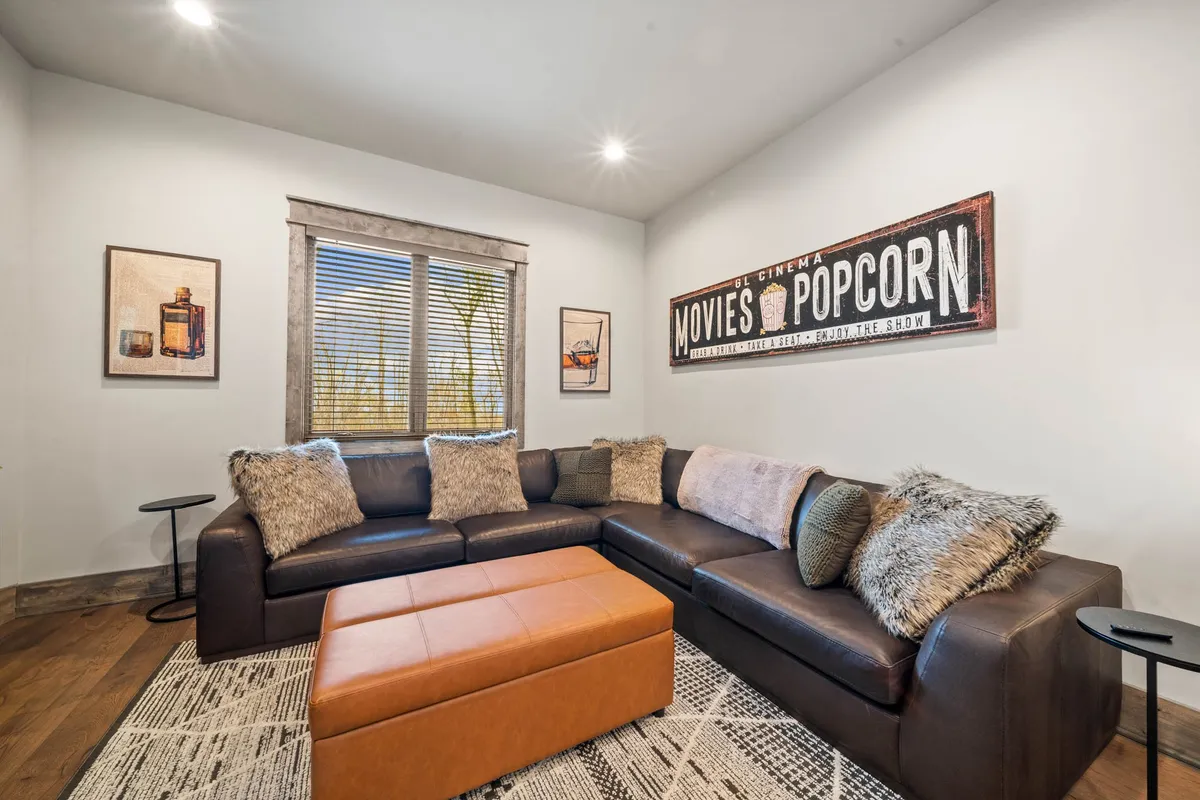 This cozy room includes a large sectional sofa, popcorn-themed wall art, and a colorful ottoman. The setup is ideal for watching movies, relaxing with friends, or enjoying board games, emphasizing comfort and casual gatherings.