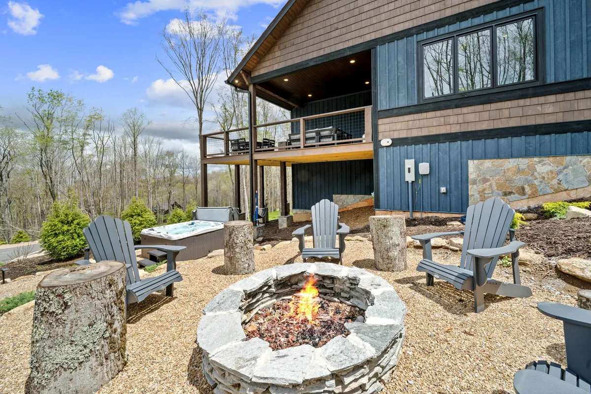 This image captures an inviting outdoor area featuring a fire pit, a hot tub, a spacious deck, and lush surrounding trees. The setup is ideal for evening gatherings, socializing, and stargazing, creating a sense of relaxation and togetherness in a mountain setting.
