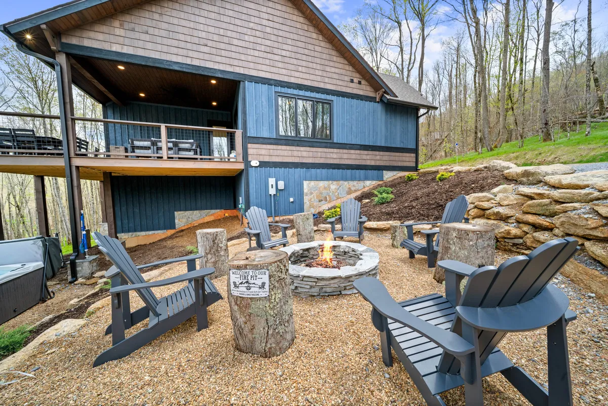 A cozy outdoor setup with a fire pit surrounded by Adirondack chairs on a wooden deck, overlooking a landscaped hillside. The scene is set for evening gatherings, with the inviting glow of the fire promising s’mores and shared stories under the stars.