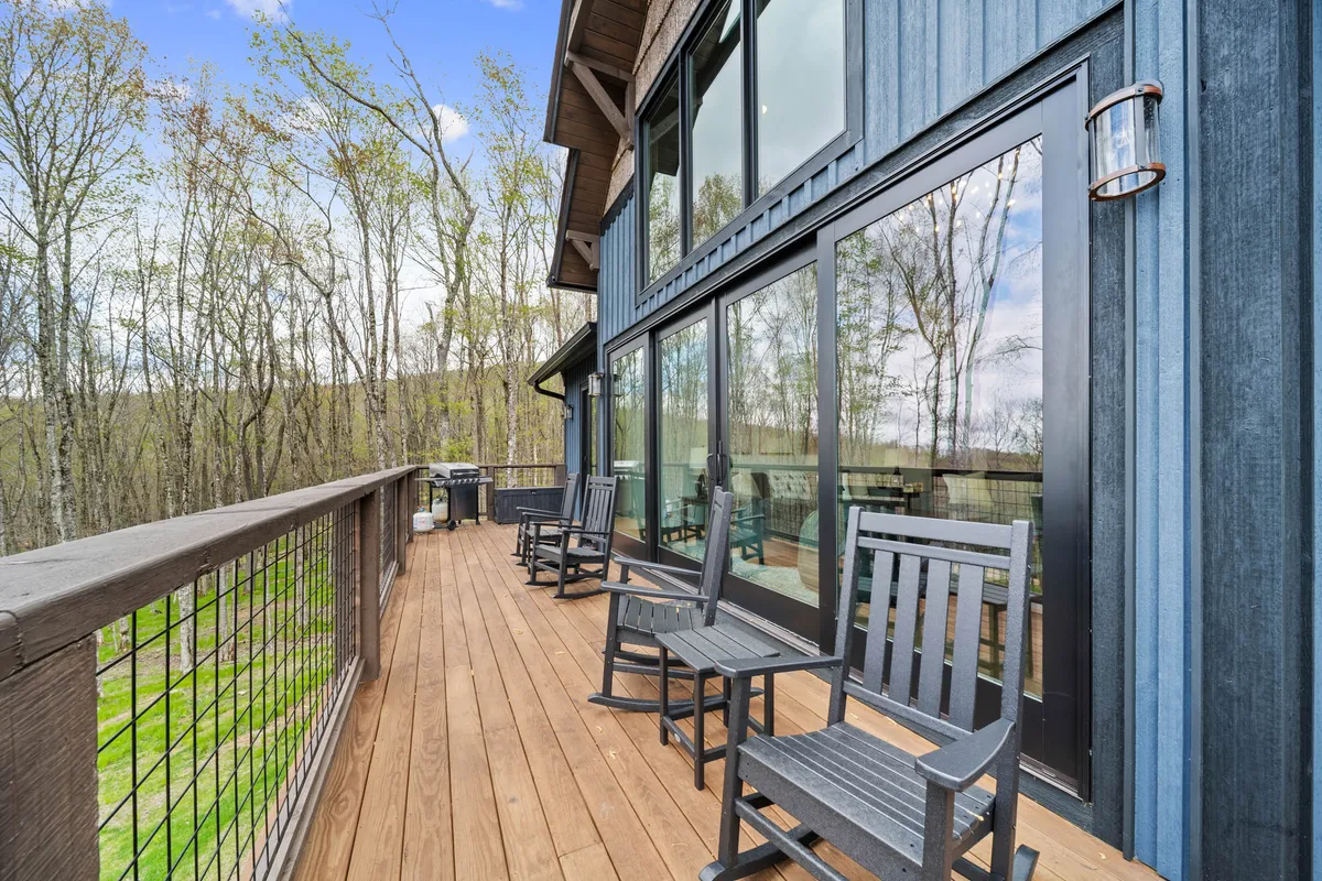 This image displays a welcoming deck with rocking chairs, a grill area, and expansive views of the surrounding nature. The combination of seating and grilling facilities suggests a perfect space for morning coffee, casual gatherings, or evening BBQs.
